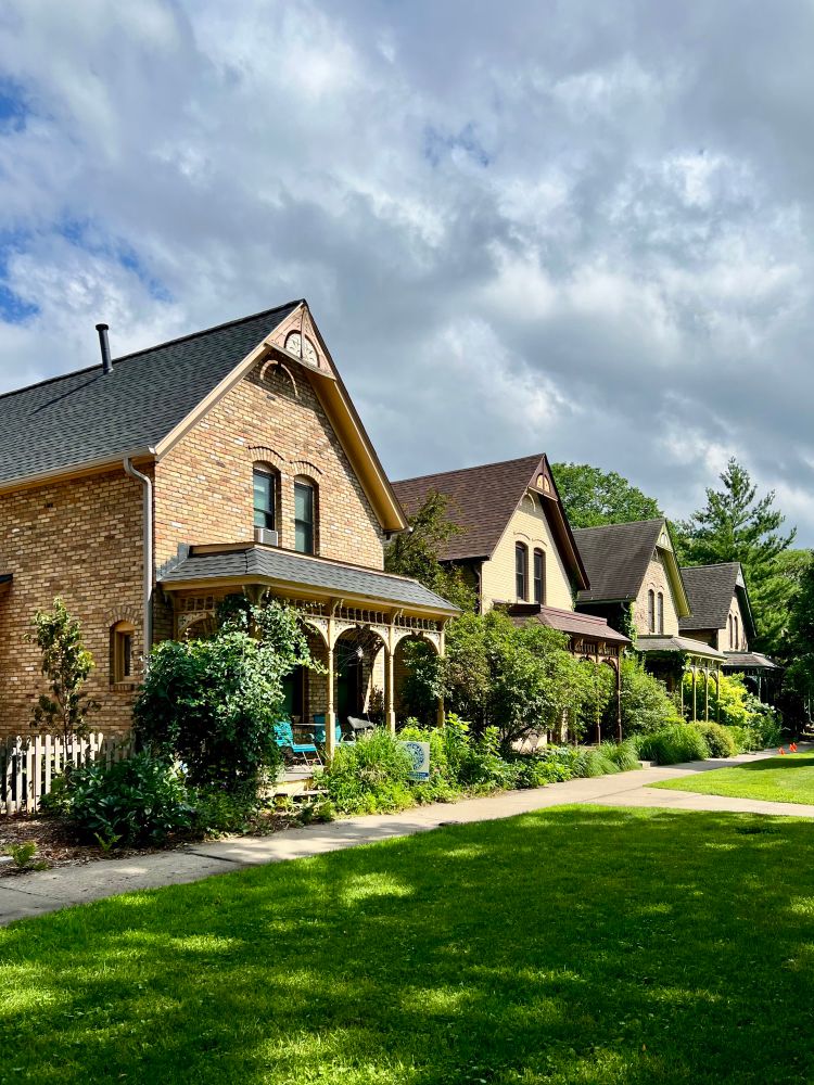 Row of front gabled brick houses in a row with large swaths of grass in front of them.