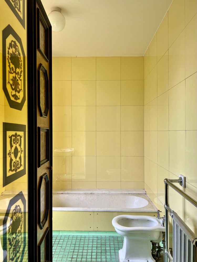 A yellow tiled bathroom with a tub and toilet. The floor is covered in blue tiles.