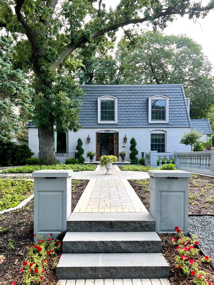 Light purple house with mansard roof at the end of a long walkway and set of steps.