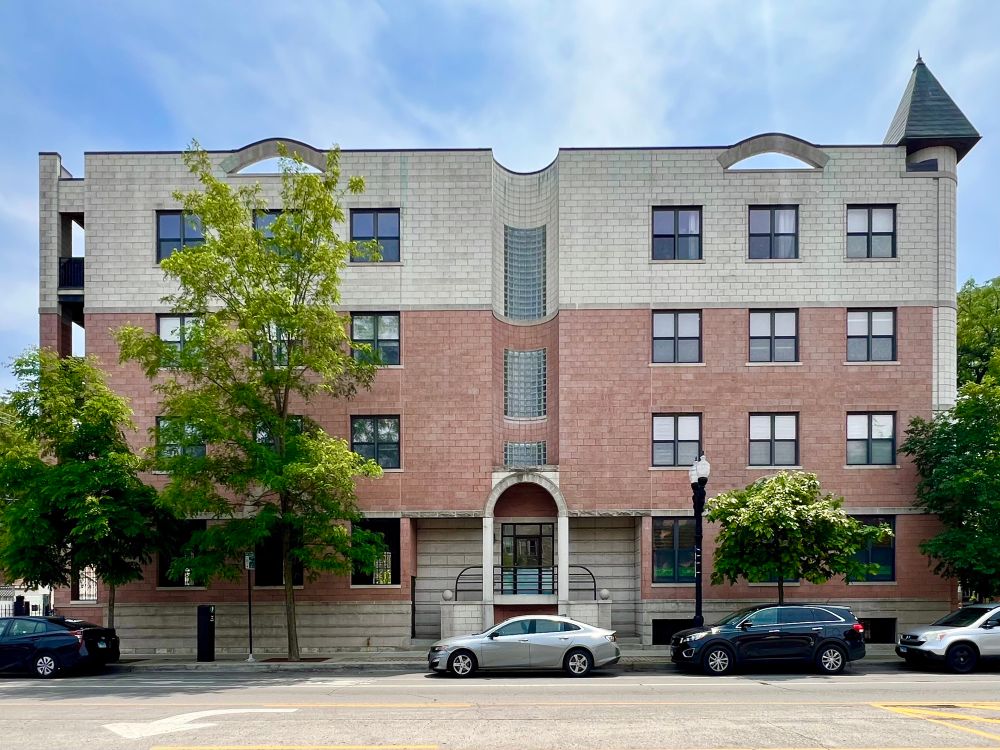 Apartment building face with cream and salmon-colored concrete blocks. The cornice has false arches and a simplified corner turret.