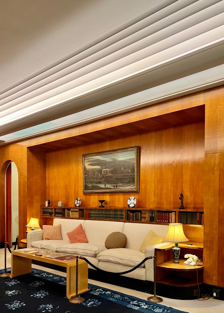 A long sofa set within a recessed cove on a wood-paneled wall. The ceiling above is stepped at its edges.