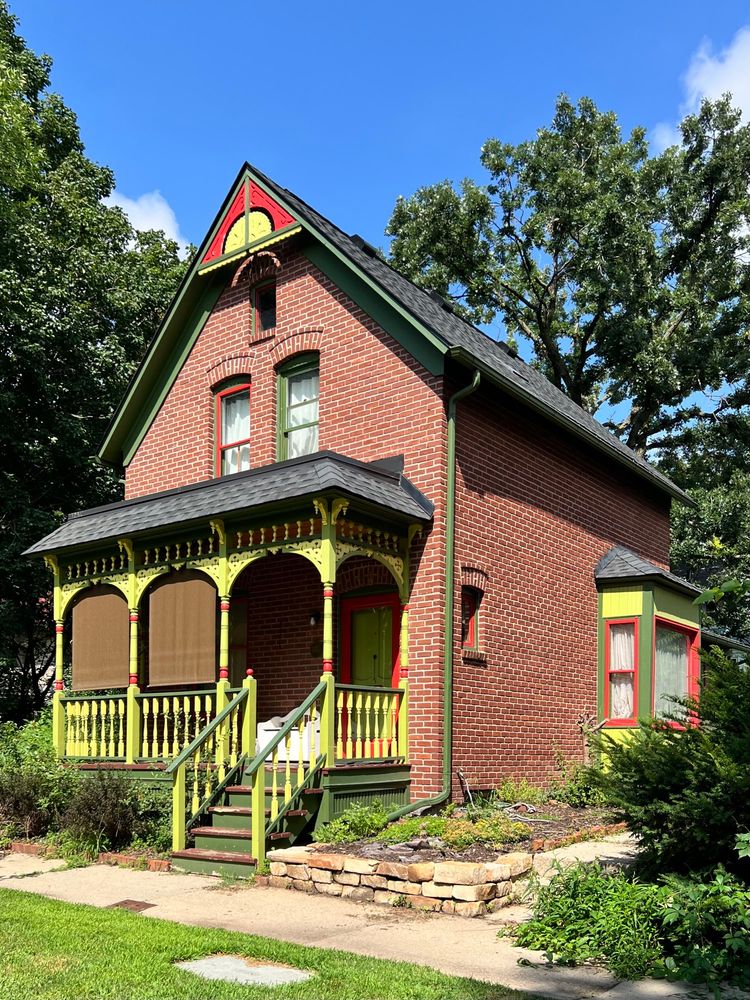 A front gabled brick house with red and lime green details on the porch and roofline.
