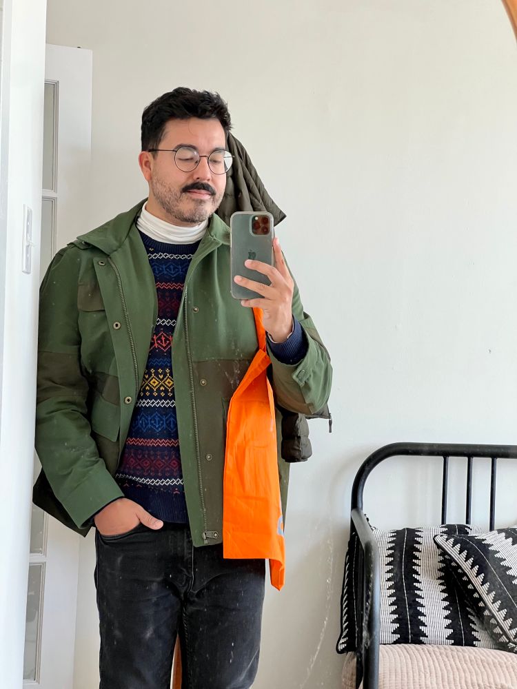 Man wearing green jacket with an orange tote bag over his shoulder.