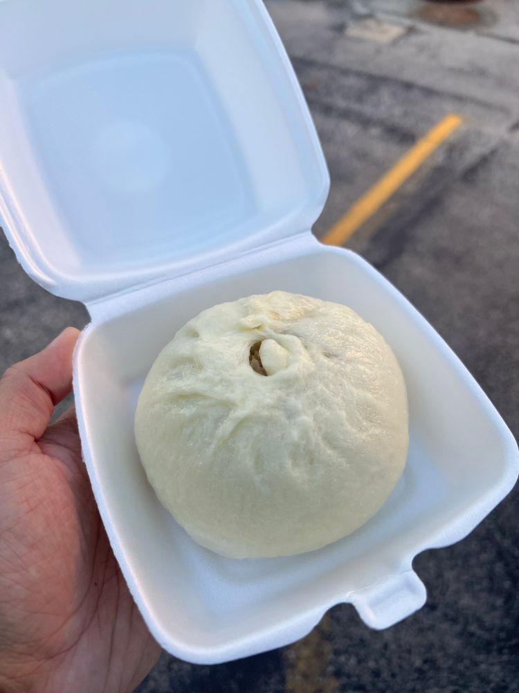 A very large and round steamed dumpling in a styrofoam container. 