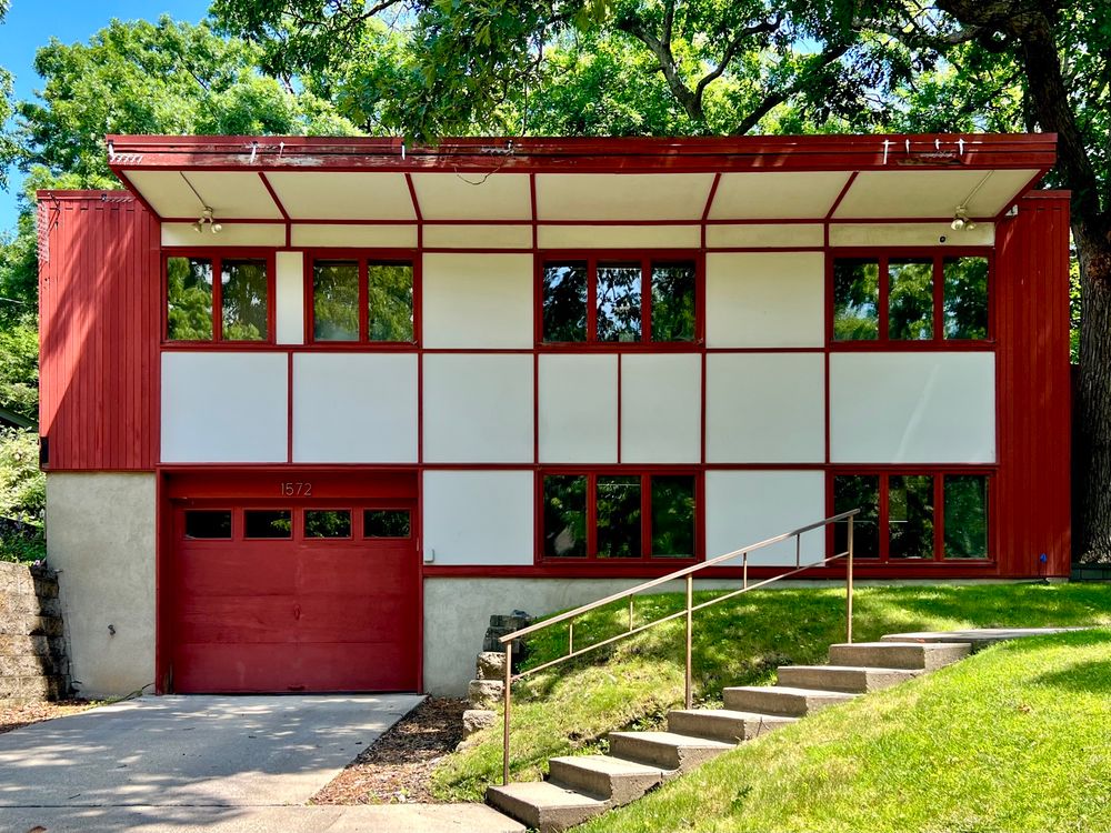Two-story midcentury house with a red, gridded exterior and large top-floor overhang.