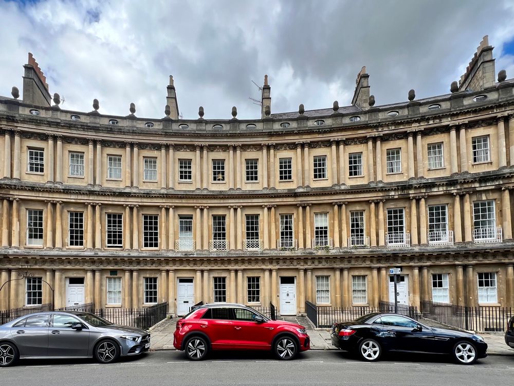 A curved row of Georgian townhomes with cars parked in front.