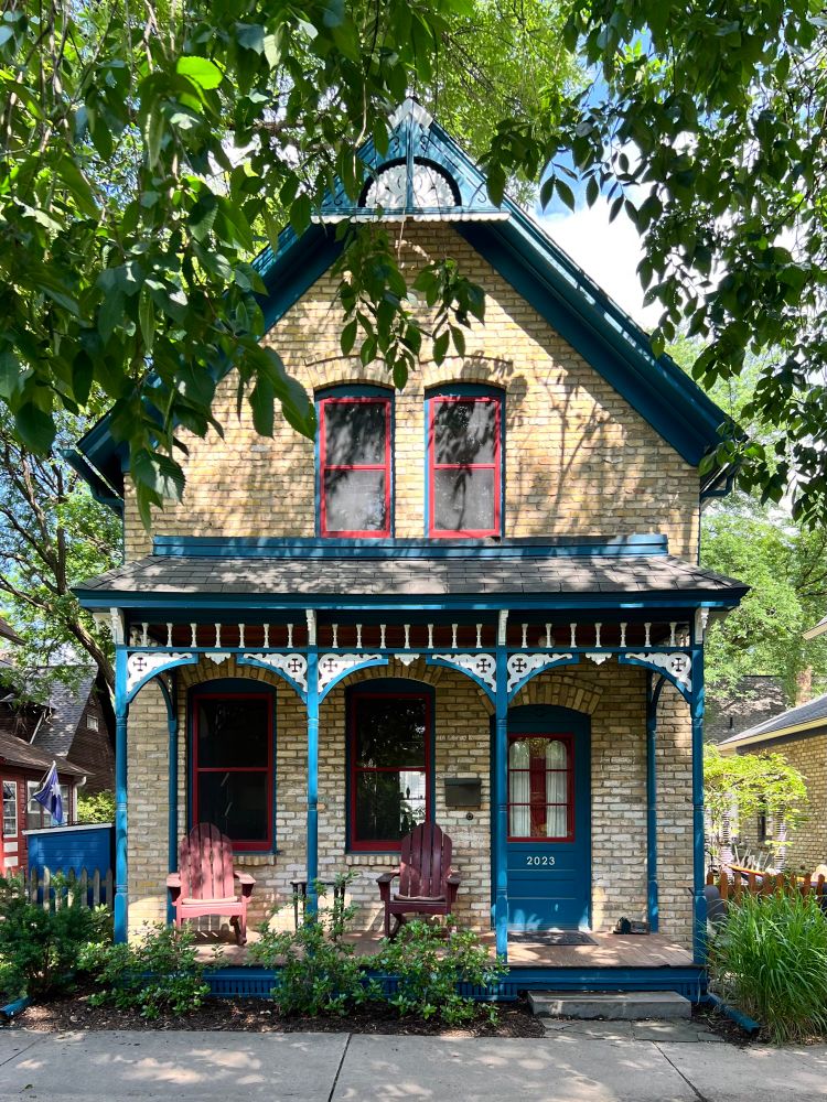 A simple two-story, front gabled house with a decorative porch featuring carved woodwork.