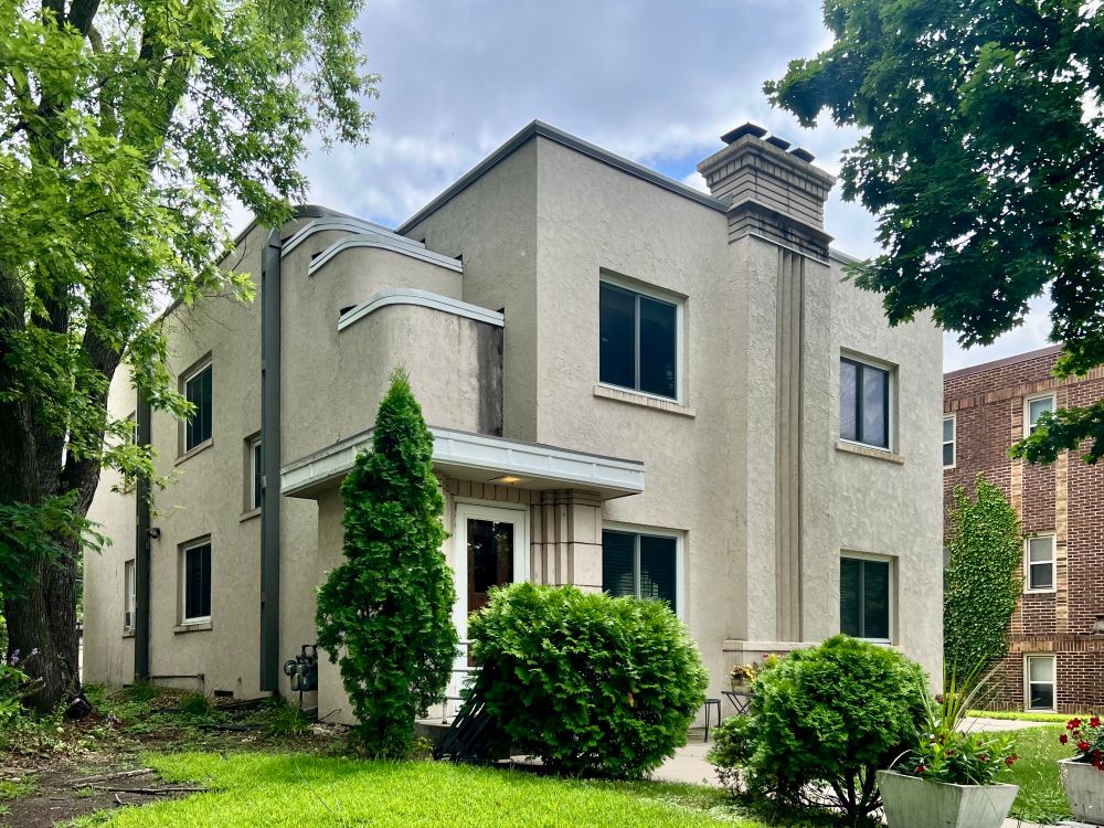 Boxy stucco duplex with a fluted chimney, recessed doorway, and stepped walls above the entrance.