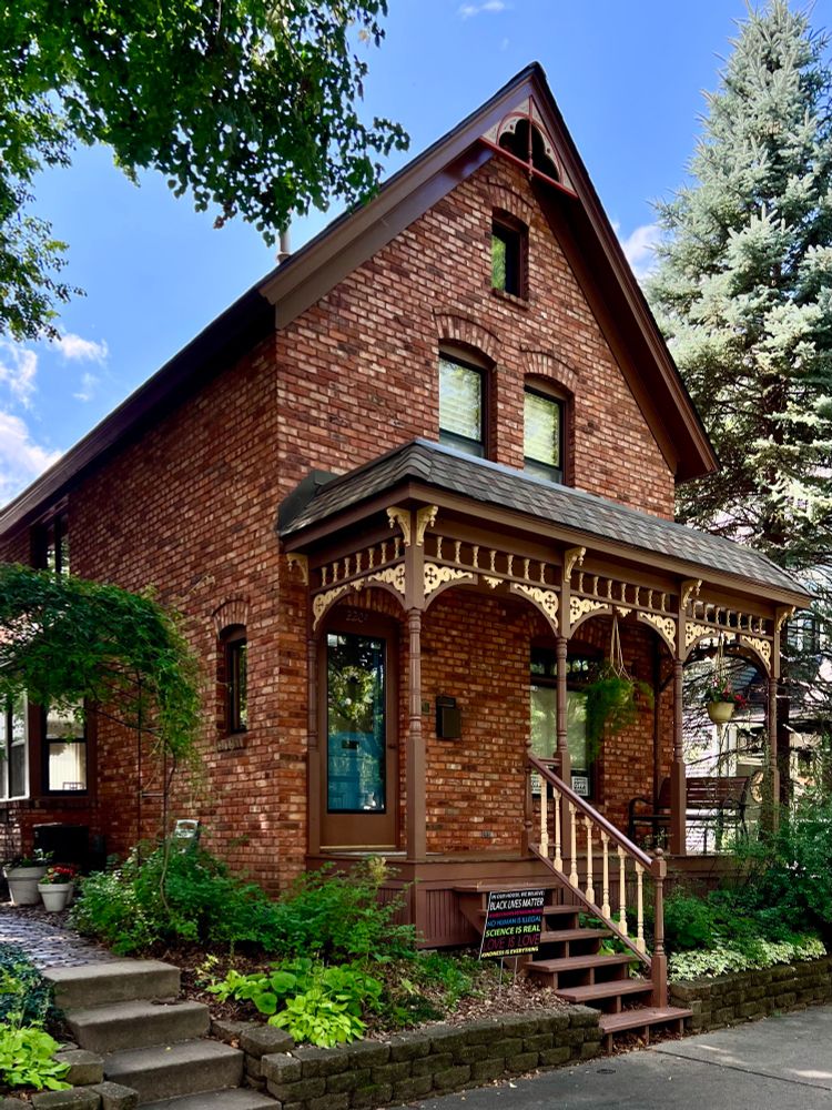 A front gable brick house with an ornate wood porch.