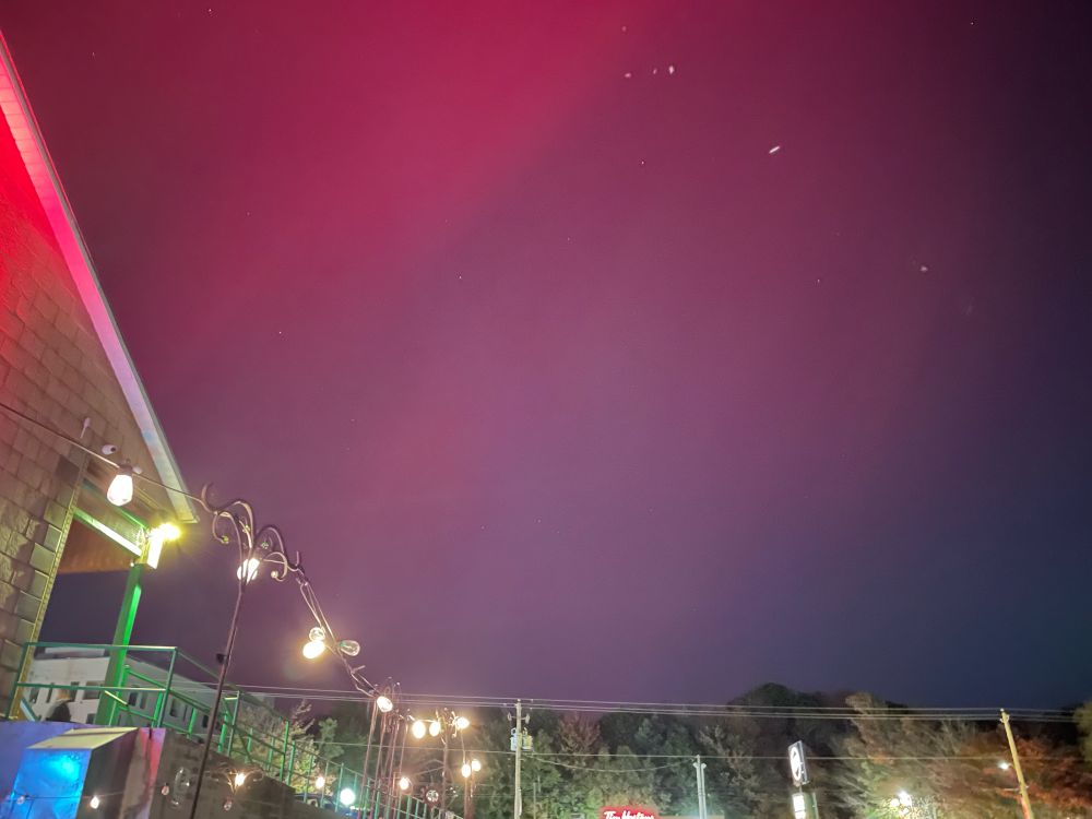 Purple aurora waves in the sky over a well-lit building, showing that the event was bright enough to see through the city light pollution.
