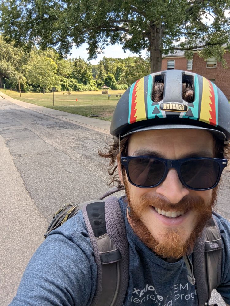 a selfie of me on my bike going through a sunny park. I'm wearing a helmet, sunglasses, and a backpack.