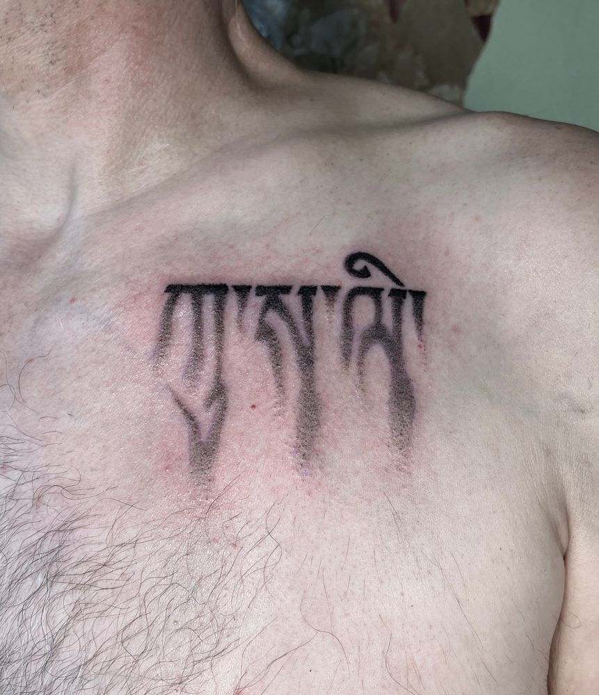 A black and grey tattoo on a person’s chest of a block of Tibetan text dissolving into smoke. 