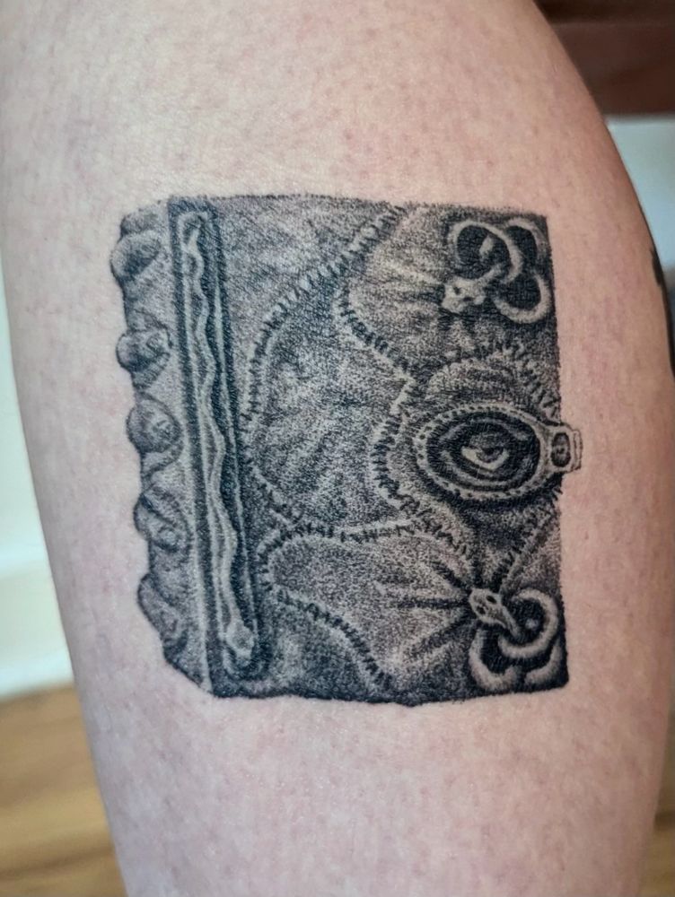 Close up of a healed black and grey tattoo of the magic book from the film Hocus Pocus on a leg. 