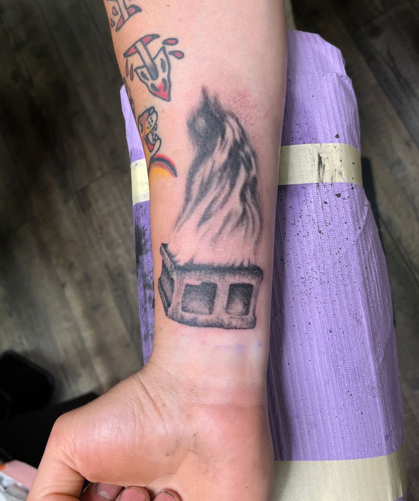 An inside wrist and forearm with a tattoo of a cinderblock on fire 
