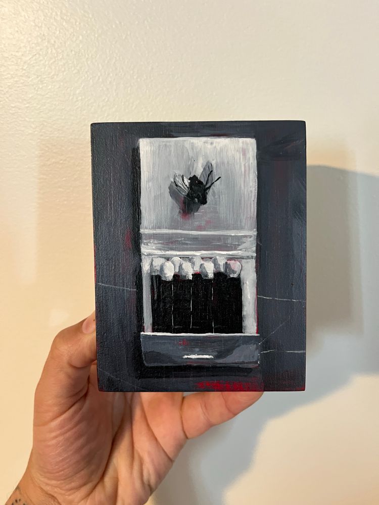A small painting on panel of a dead fly on the cover of an open match book, in front of a white wall, held by a hand in front of a wall
