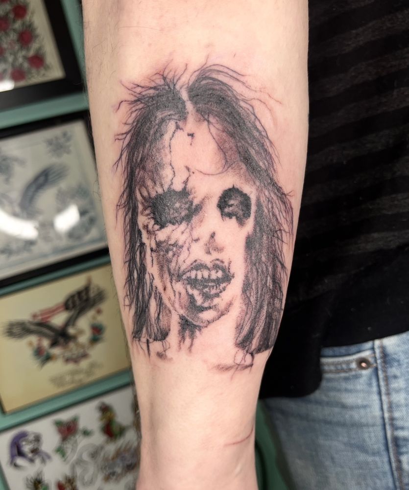Tattoo on a forearm of a Stephen Gammel illustration from Scary Stories to Tell in The Dark, seen with tattoo flash on the wall behind. 