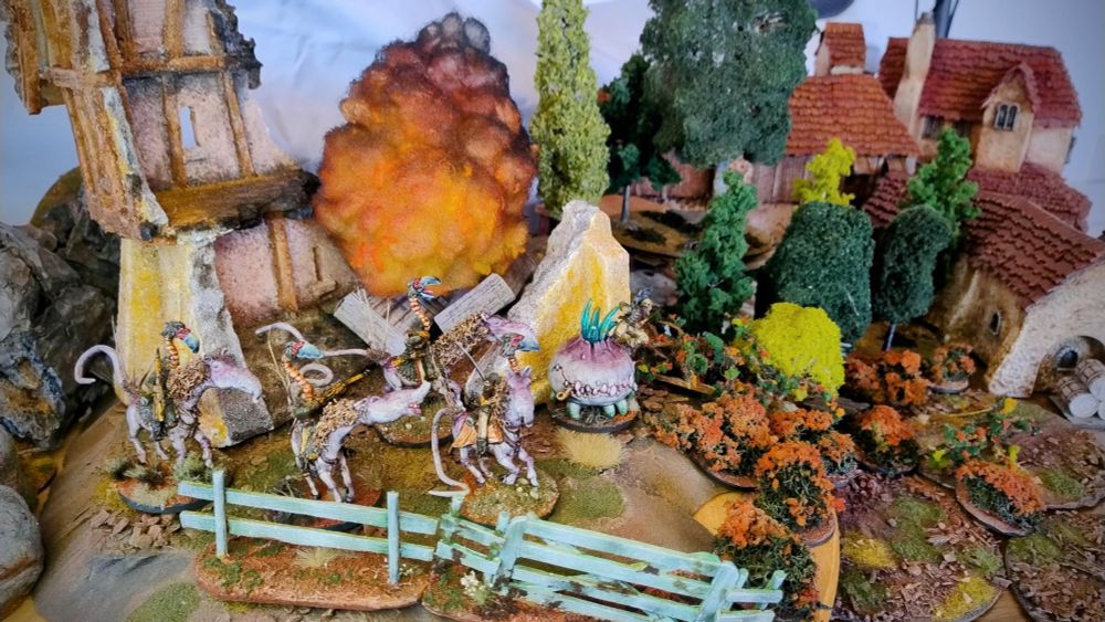 A wargaming terrain ensemble of houses and scatter terrain, burned-down or otherwise intact, being pillaged by monstrous Turnip28 horsemen.