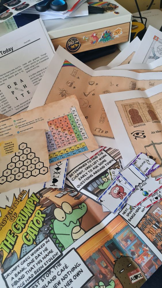 A mess of papers strewn across a desk showing components of short escape room style puzzles that can fit within a letter / small envelope.