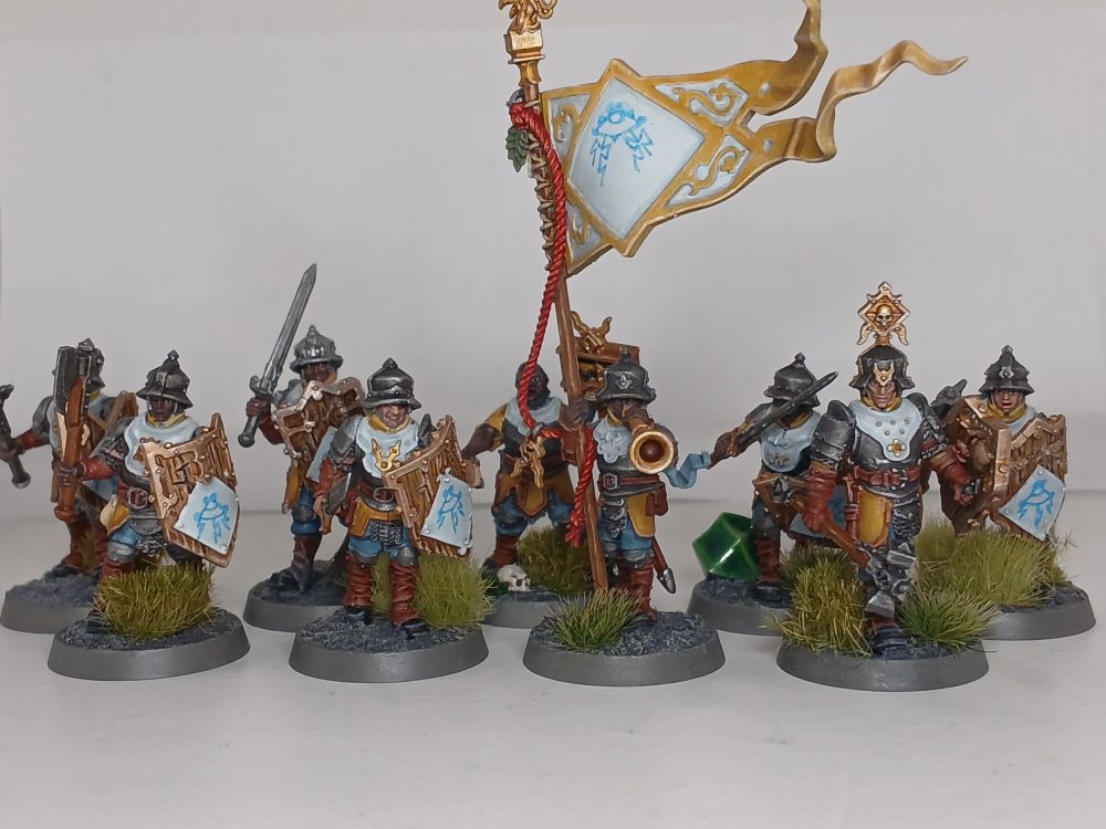 The photo depicts ten model fantasy human warriors in armour, with shields and various weapons.  One of them is holding a banner.