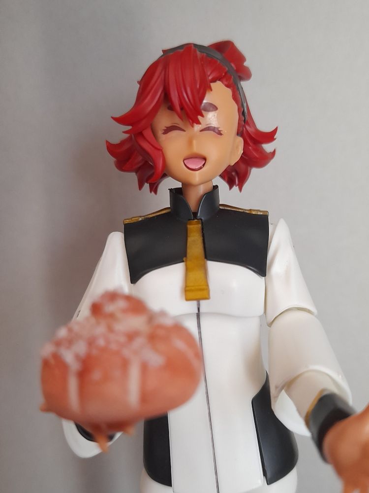 Photo of a figure of Suletta Mercury smiling and holding a toy pan de muerto 