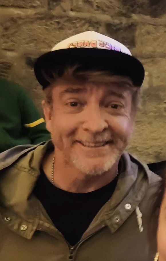 Rhys Darby wearing a cap and smiling 