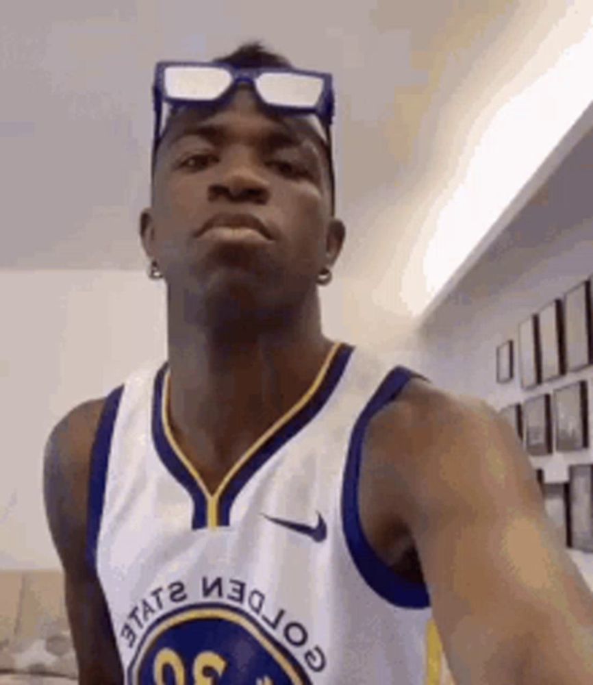 a basketball player wearing sunglasses and a golden state warriors jersey is taking a selfie .