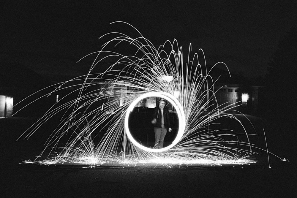 black and white photo, long exposure of a shower of sparks arcing around a bright circle