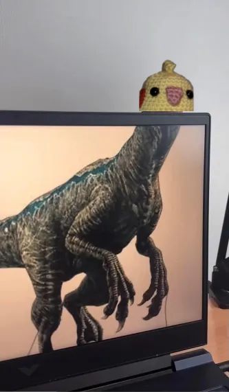 dino saurer auf einem bild schirm ohne kopf doch der kleine häkel vogel groggy balboa schaut hinter dem bild schirm her vor 