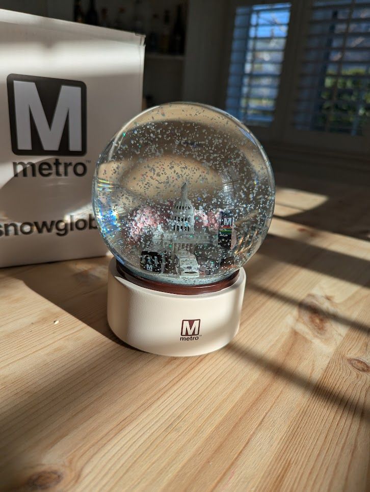 WMATA snow globe showing trains and busses in front of the Capitol Building with a Metro Pylon on the side
