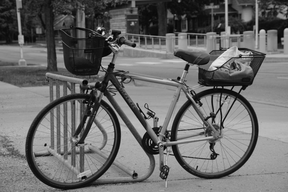 A bicycle with front and rear baskets cabled to a rack next to a city street