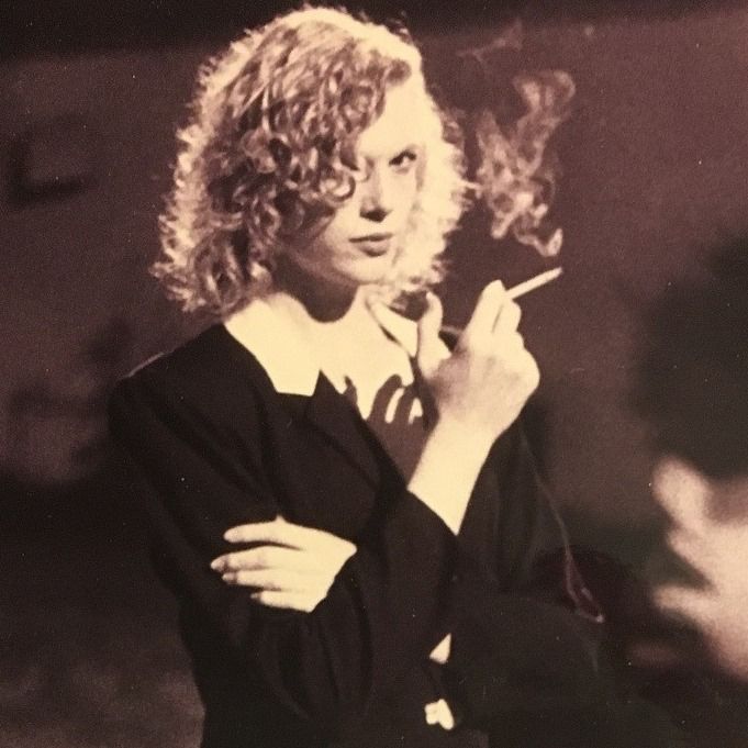 A black and white photo of a woman in a dark-colored top smoking a cigarette