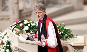 Bishop Budde is standing in front of a lectern surrounded by flowers.