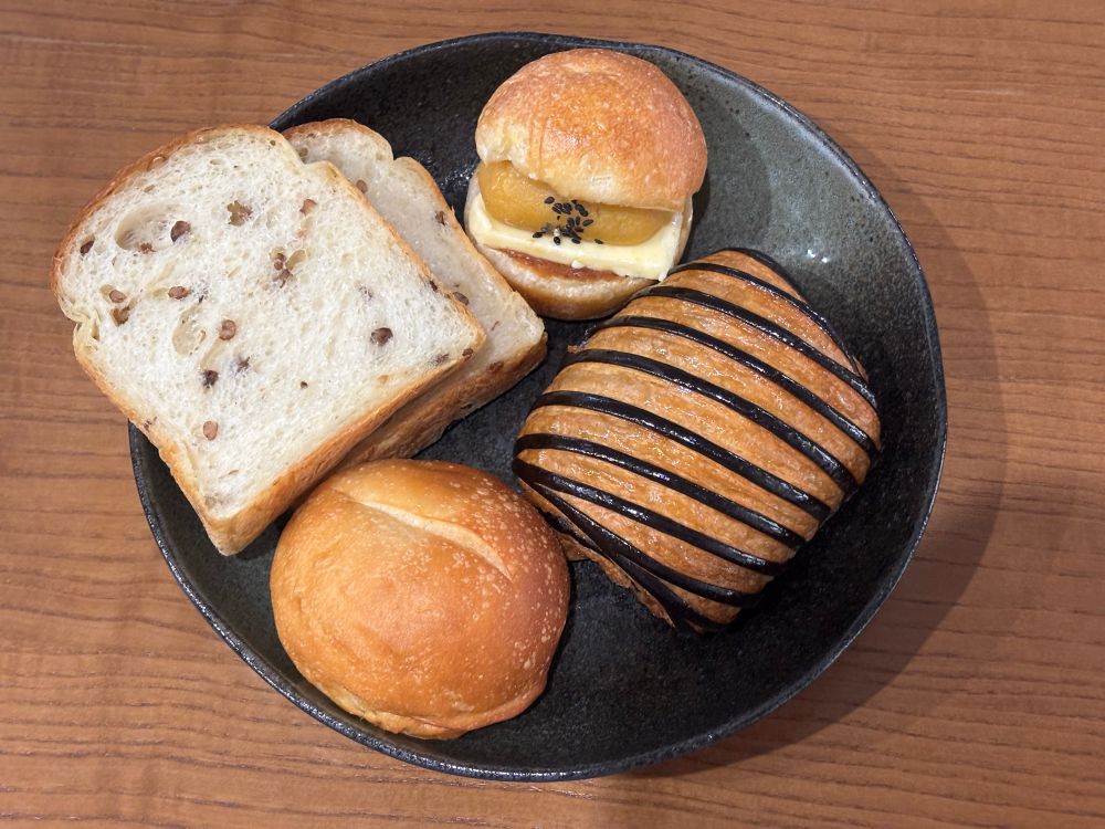 皿に乗ったパン4種
五穀ブレッド2枚、お芋あんとバターを挟んだ丸いパン、まんまるの米粉パン、ストライプ状にチョコソースが巻いてあるクロワッサン