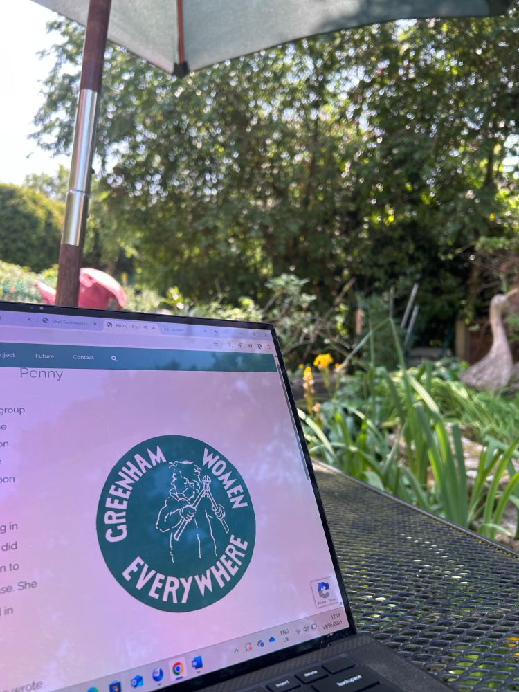 A laptop showing the ‘Greenham women everywhere’ online archive on a garden table surrounded by nature 