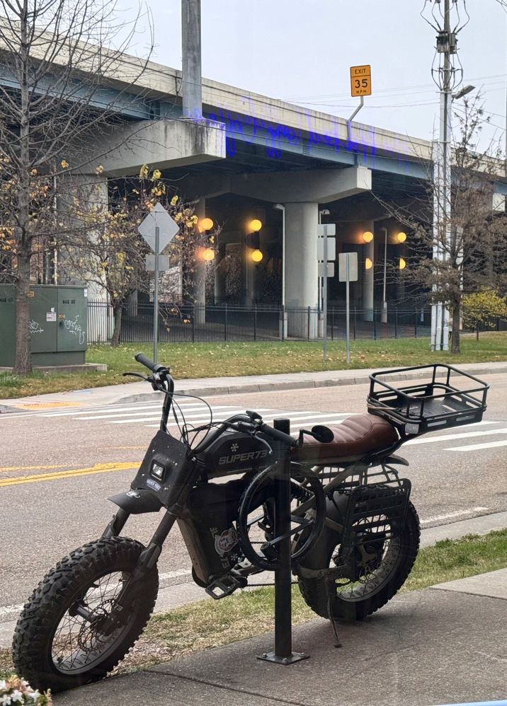 My Super73 e-bike outside a coffee shop, photographed through the window from the table where I'm typing this.