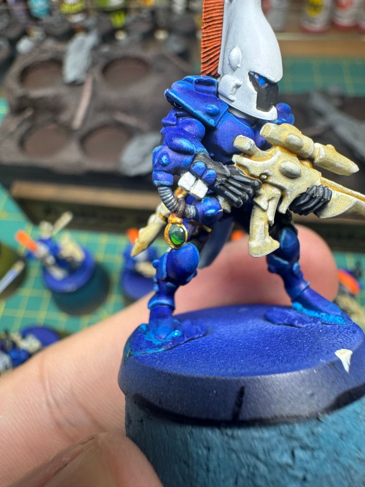 A close up image of a warhammer miniature with a painted green gemstone in a gold setting.