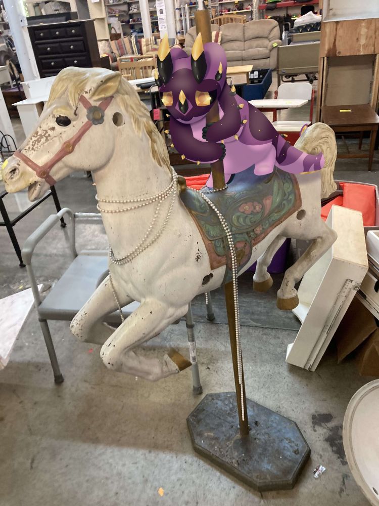 A photo of a strange horse decoration ? from a thrift store a purple katragoon with golden horns has been drawn onto it holding on for dear life, after having successfully climbed up but struggling to not fall off
