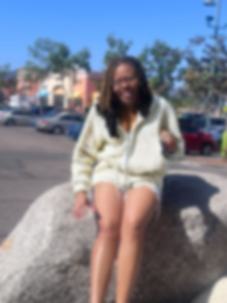 Me sitting on a rock in a beige hoodie blurred