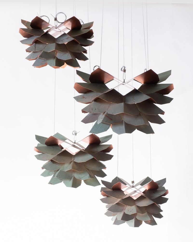 Four pinecone-like pendants made from folded pieces of reclaimed roofing copper.