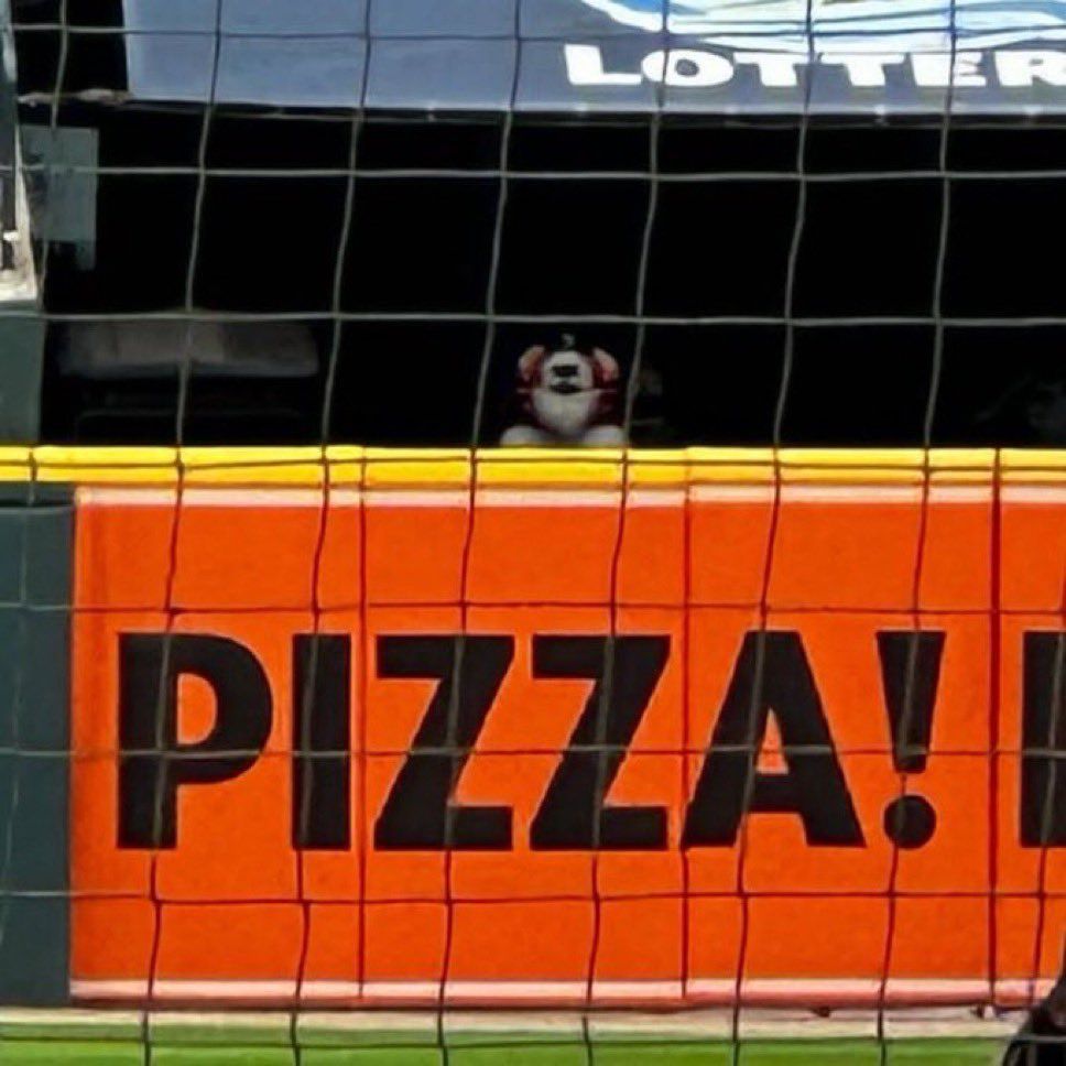 A far shot of the DetroitTigers mascot, Paws, standing in the alley at Comerica Park. There is a large PIZZA! sign in front of him.