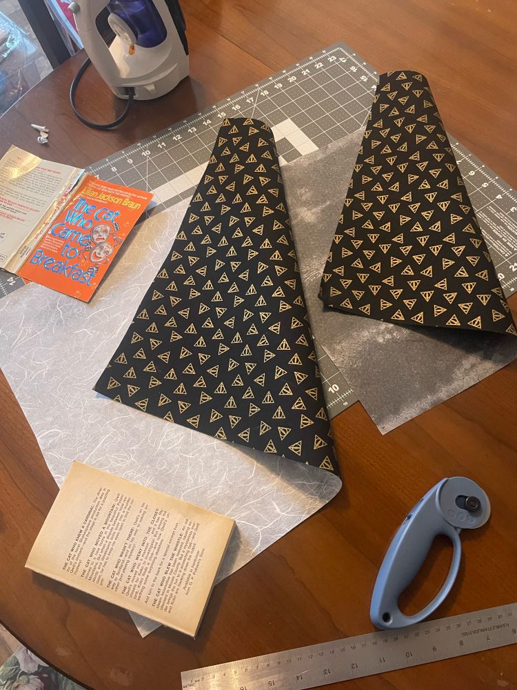 Two pieces of cloth with paper backing paperback book with cover removed and a rolling cutter in lower corner 