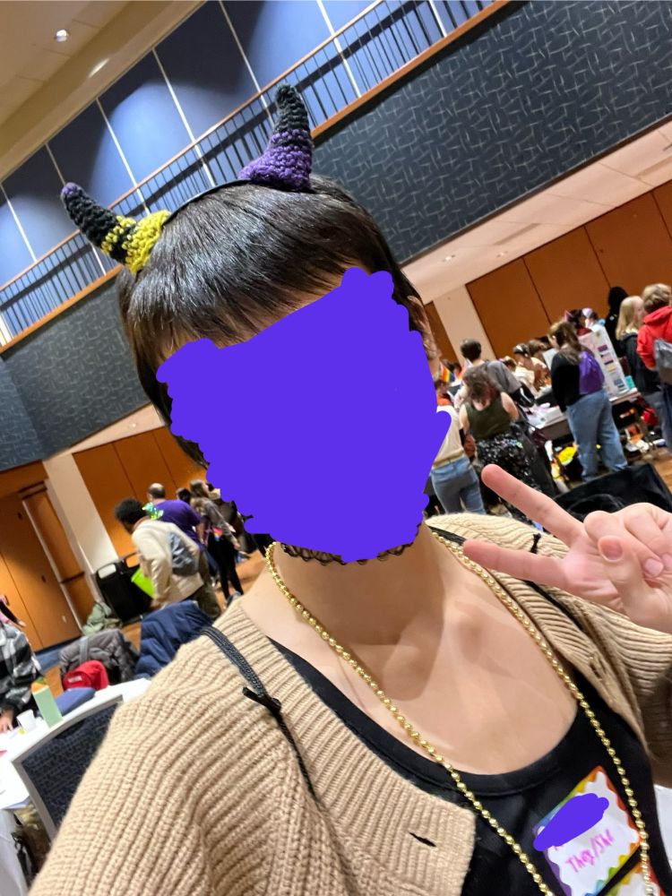a picture of me (with my face censored with purple scribbles) wearing black (one has purple stripes, the other has yellow stripes) crochet horns
