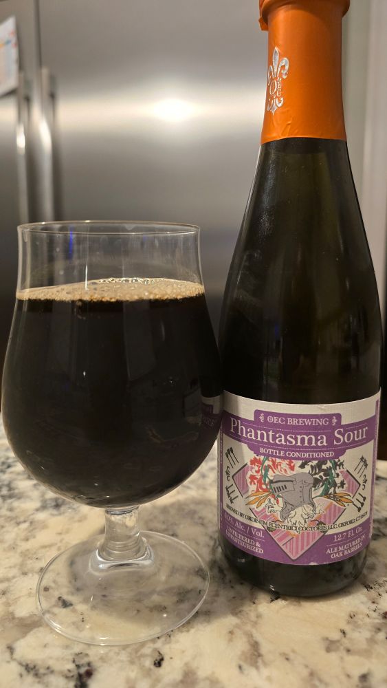 Jet black beer in a glass next to a bottle with a purple label.