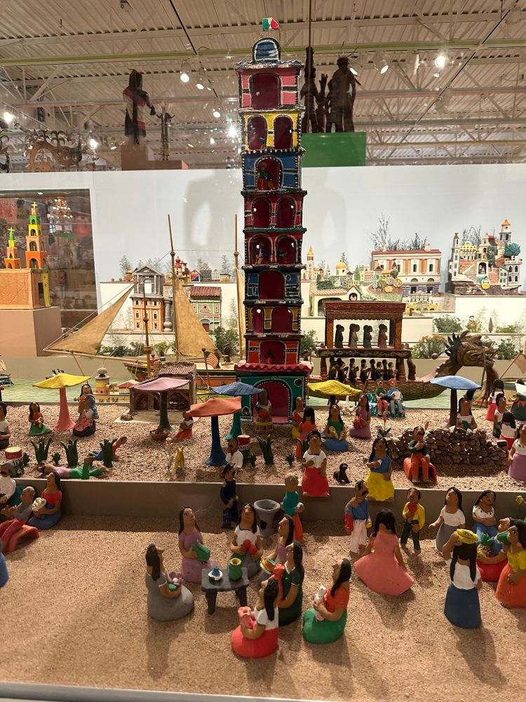 a diorama of a town square made from figurines from Mexico. There's a large tower in the middle and tiny carvings of people hanging out around it