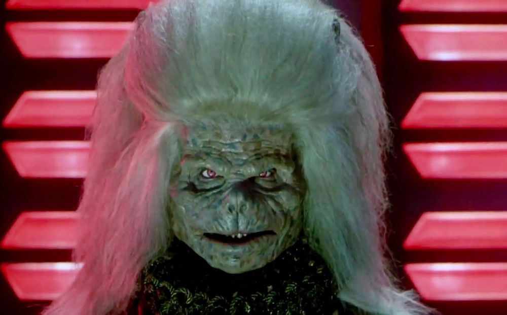 A picture of actor Robert Towers wearing a large white wig that has a massive pompadour with a creepy monster face as the character Karg in the 1987 movie Masters of the Universe. 