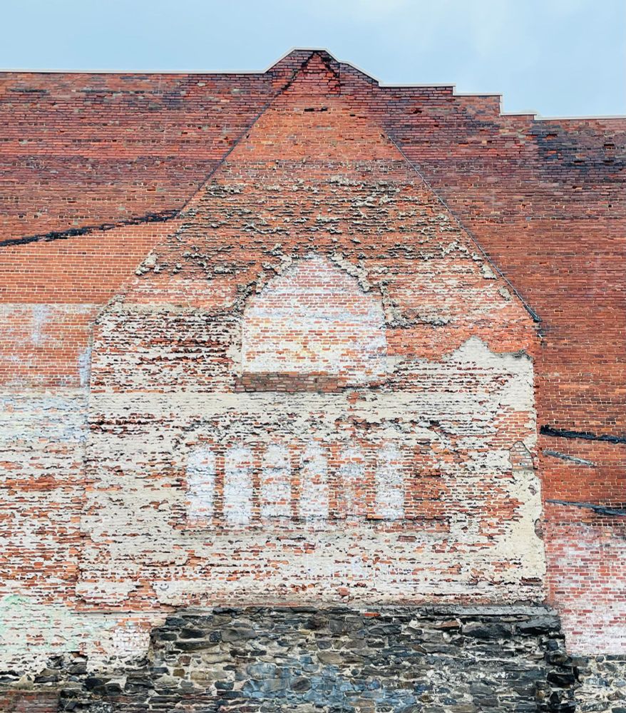 The shape and fenestration of a former building can be seen on a brick wall.