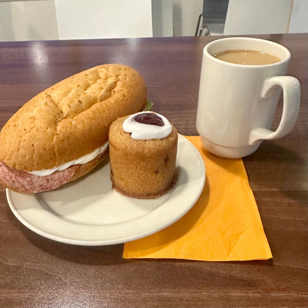 Lautasella sämpylä ja runebergintorttu, vieressä kuppi kahvia.