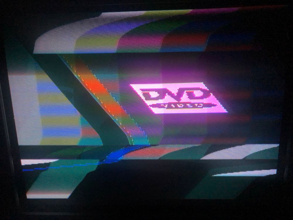 photo of my 90s Panasonic CRT TV displaying two video sources over the top of each other - colour bars and an NES demake of the bouncing DVD logo
