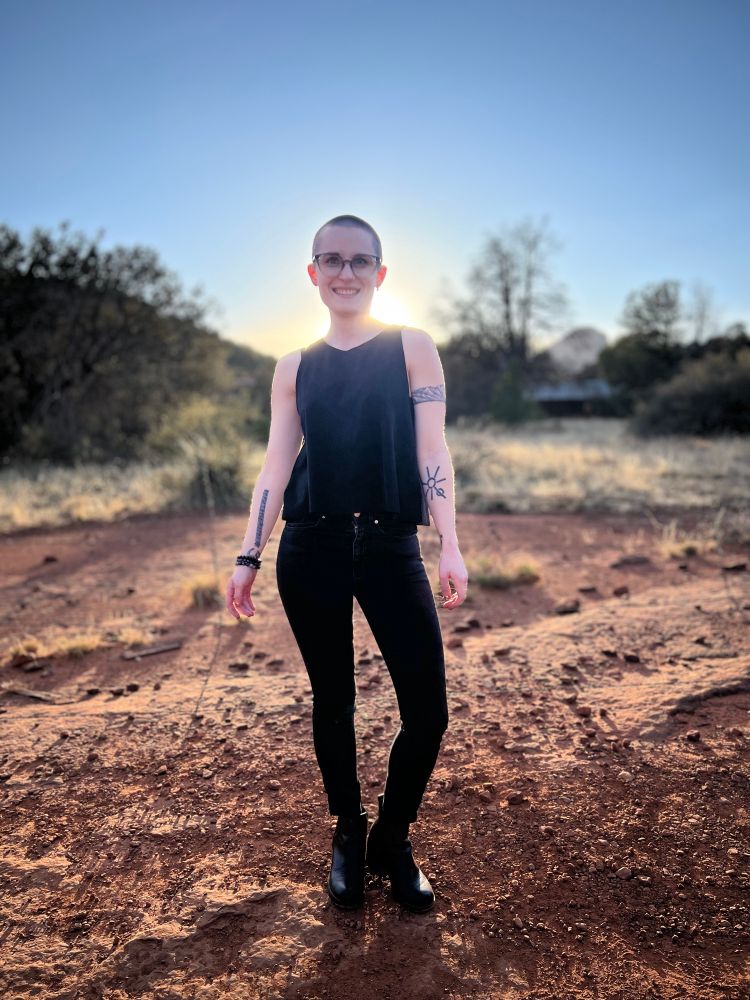 Skyler in all black with the sun glowing behind them on a desert landscape