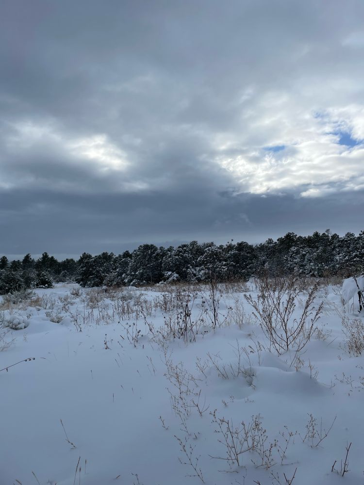 A gray cloudy sky with a small blue hole. Landscape covered in snow in the foreground. 